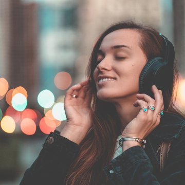 bluetooth wireless wired headphones woman long hair happy closed eyes listening to music on headphones city lights in the background